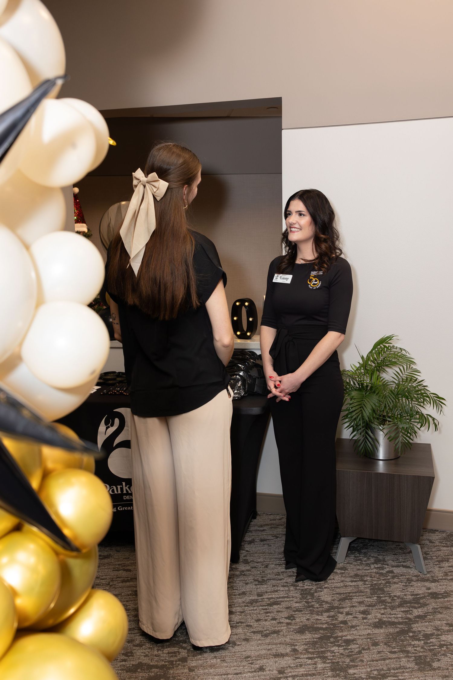 Two staff members in black uniforms having a conversation near event decorations.