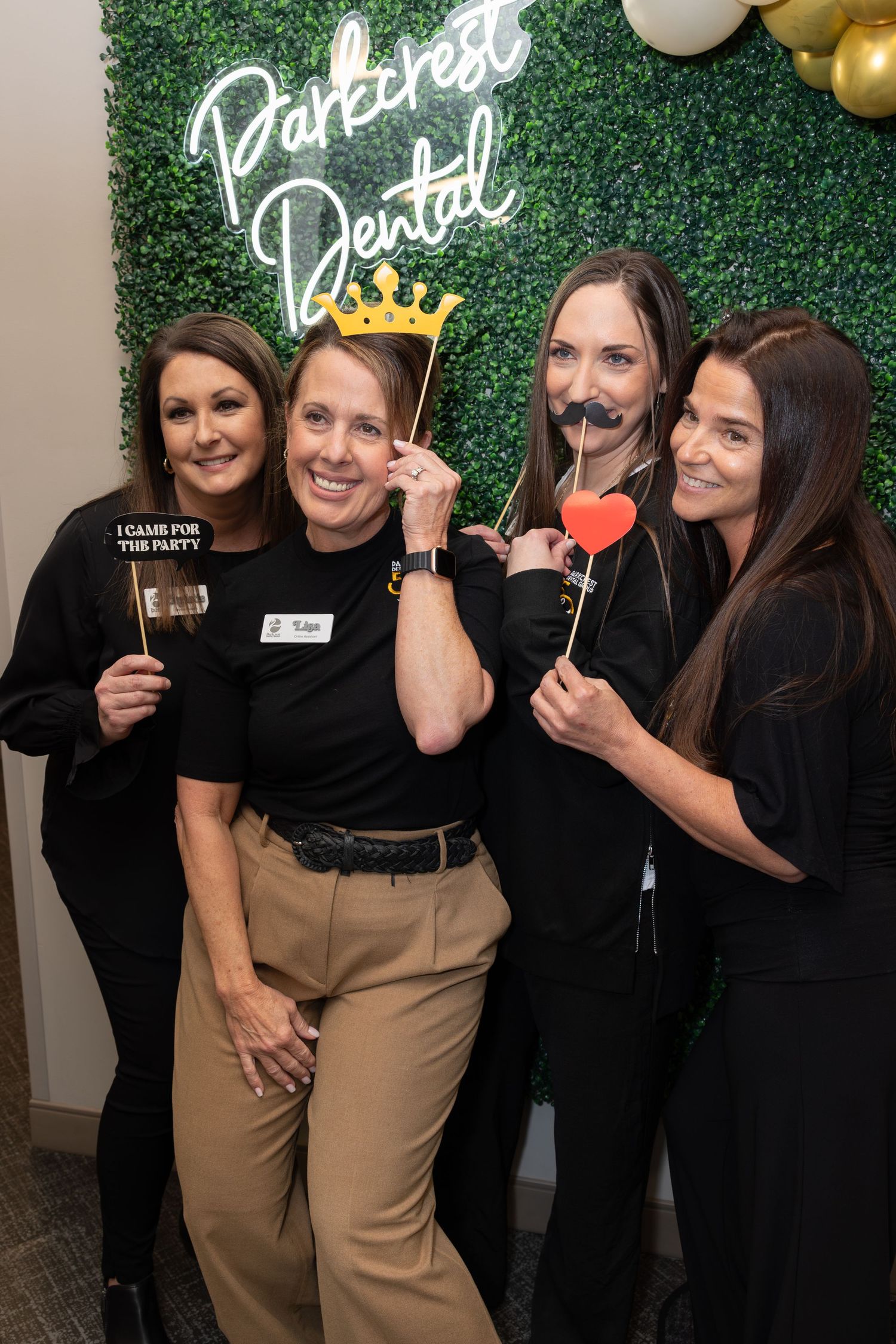 Staff members pose with photo props in front of a green wall with neon dental office signage.