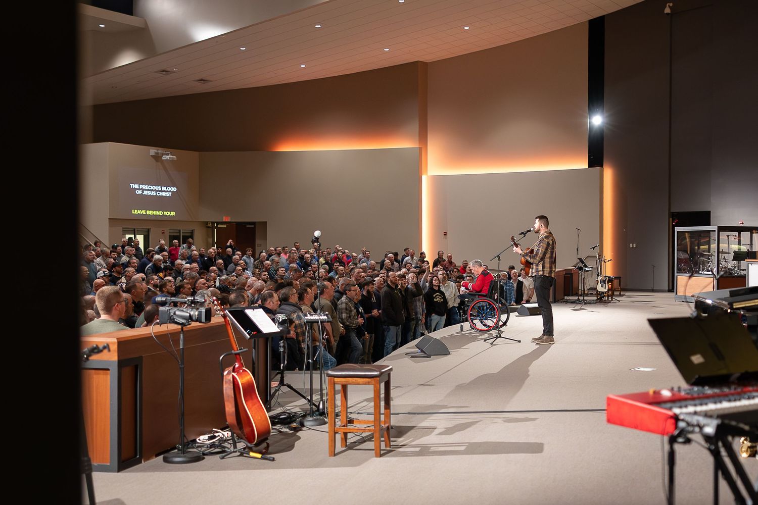Musicians and performers on stage during a concert in a modern auditorium with warm lighting and a full audience.