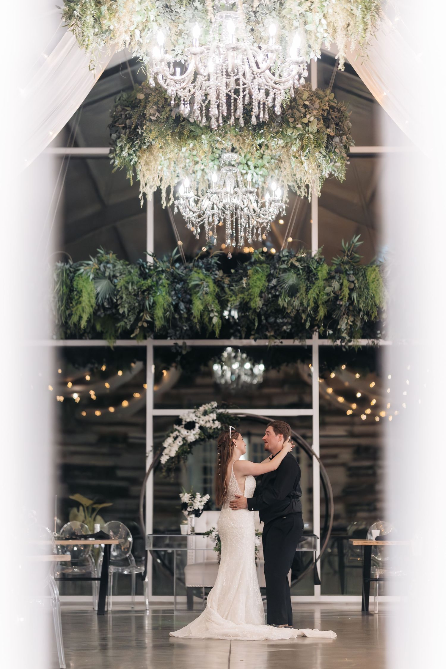 Couple shares romantic dance under elegant crystal chandelier and greenery-adorned ceiling.