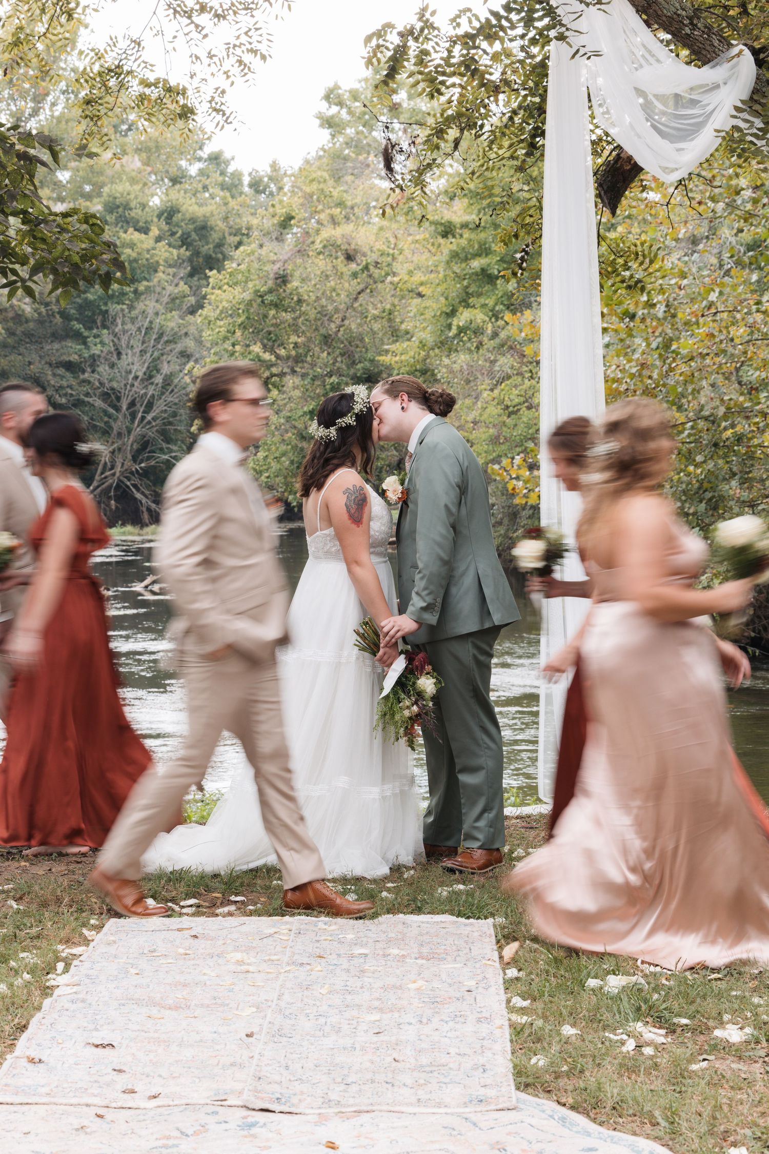 Wedding ceremony with guests in motion around couple sharing moment under white arch.