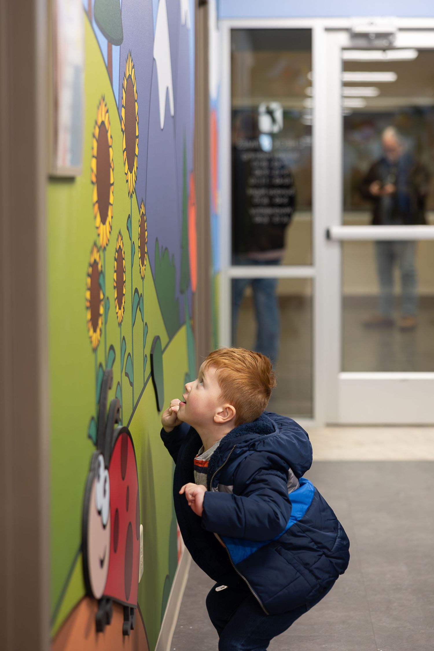 A young boy examining a colorful wall mural with a painted sunflower design.