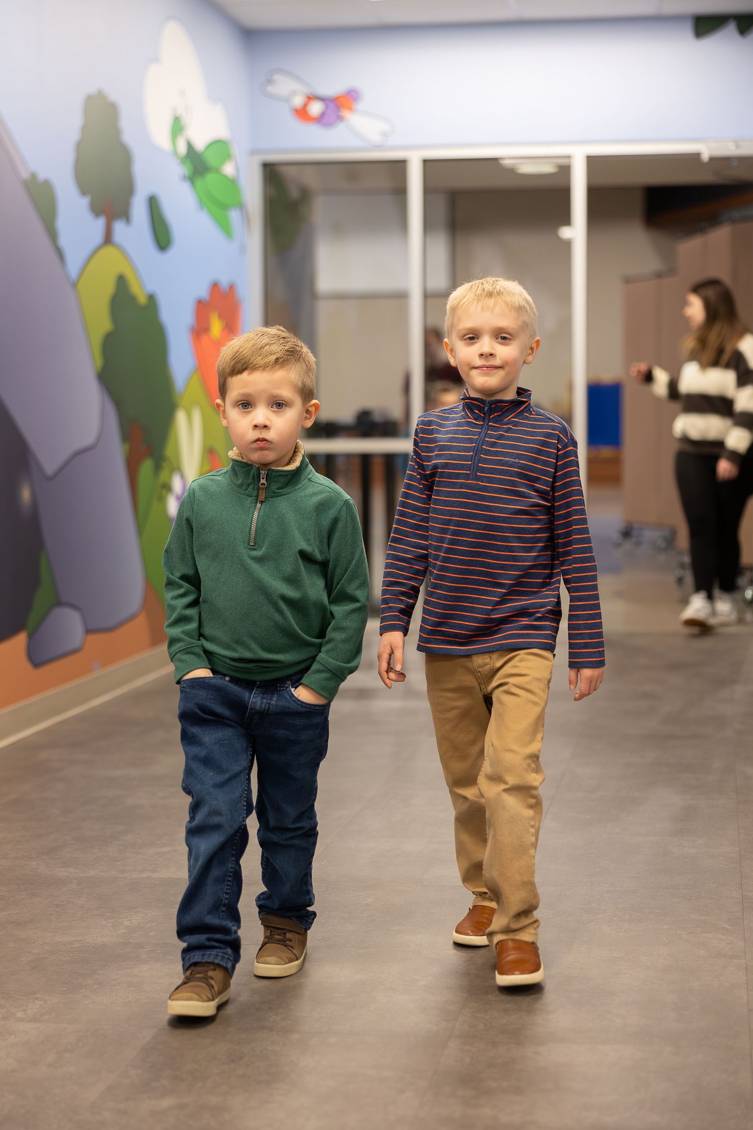 Two young students walk together in a hallway decorated with nature-themed murals.