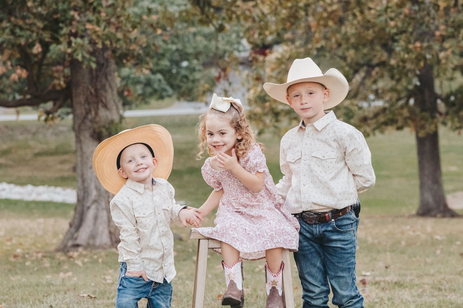Three children in western wear pose together outdoors during autumn.