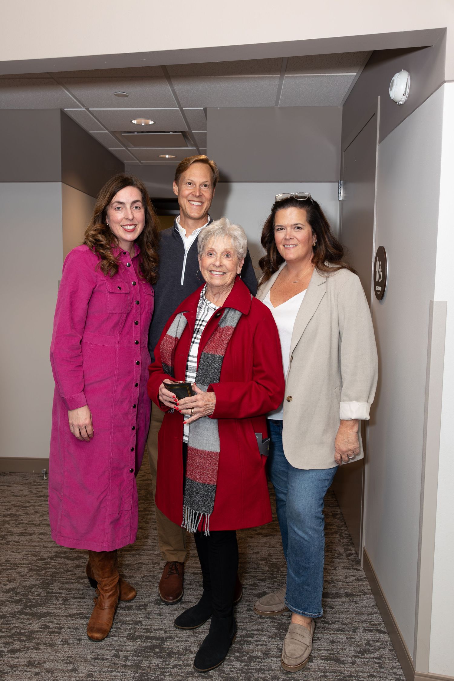 Group gathered in hallway with person wearing bright pink dress and red coat.