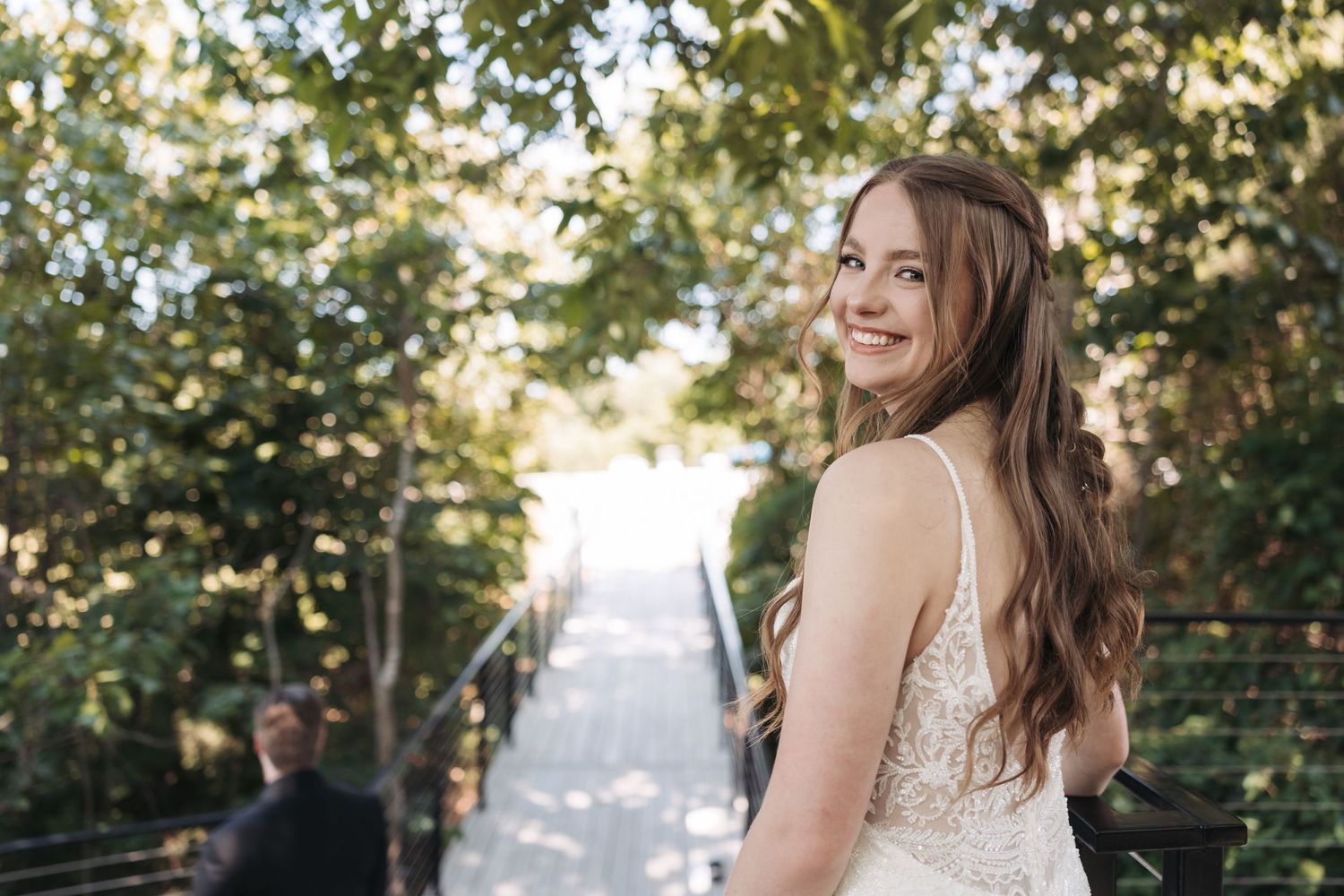 A bride in a white dress poses on an outdoor pathway surrounded by lush greenery.