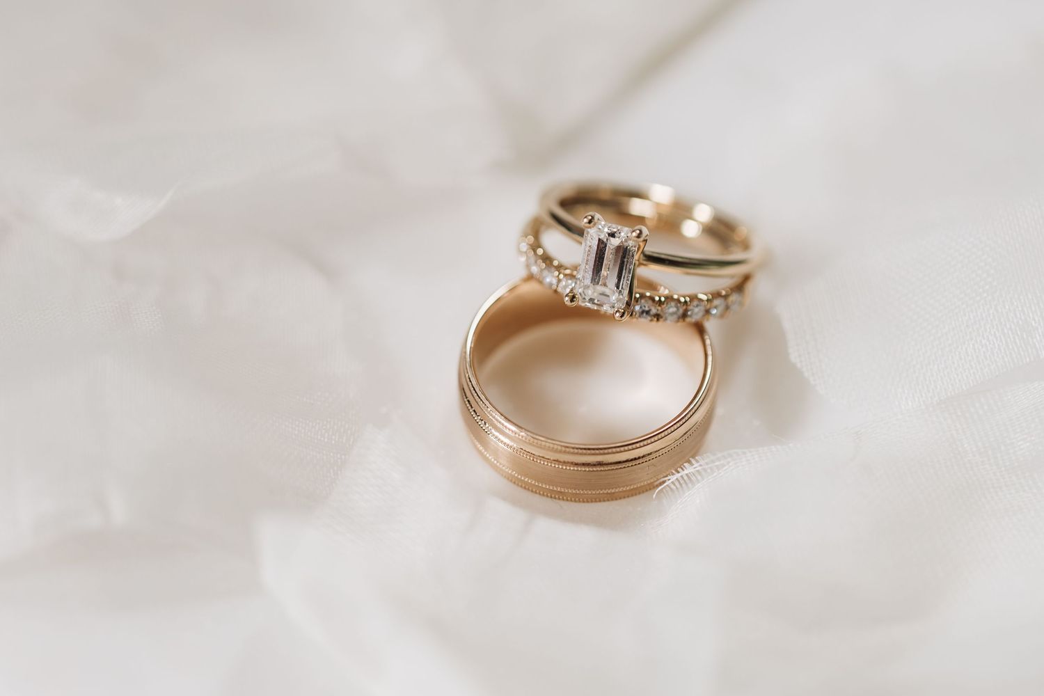 Two wedding rings, one diamond engagement ring and one gold band, on white fabric.