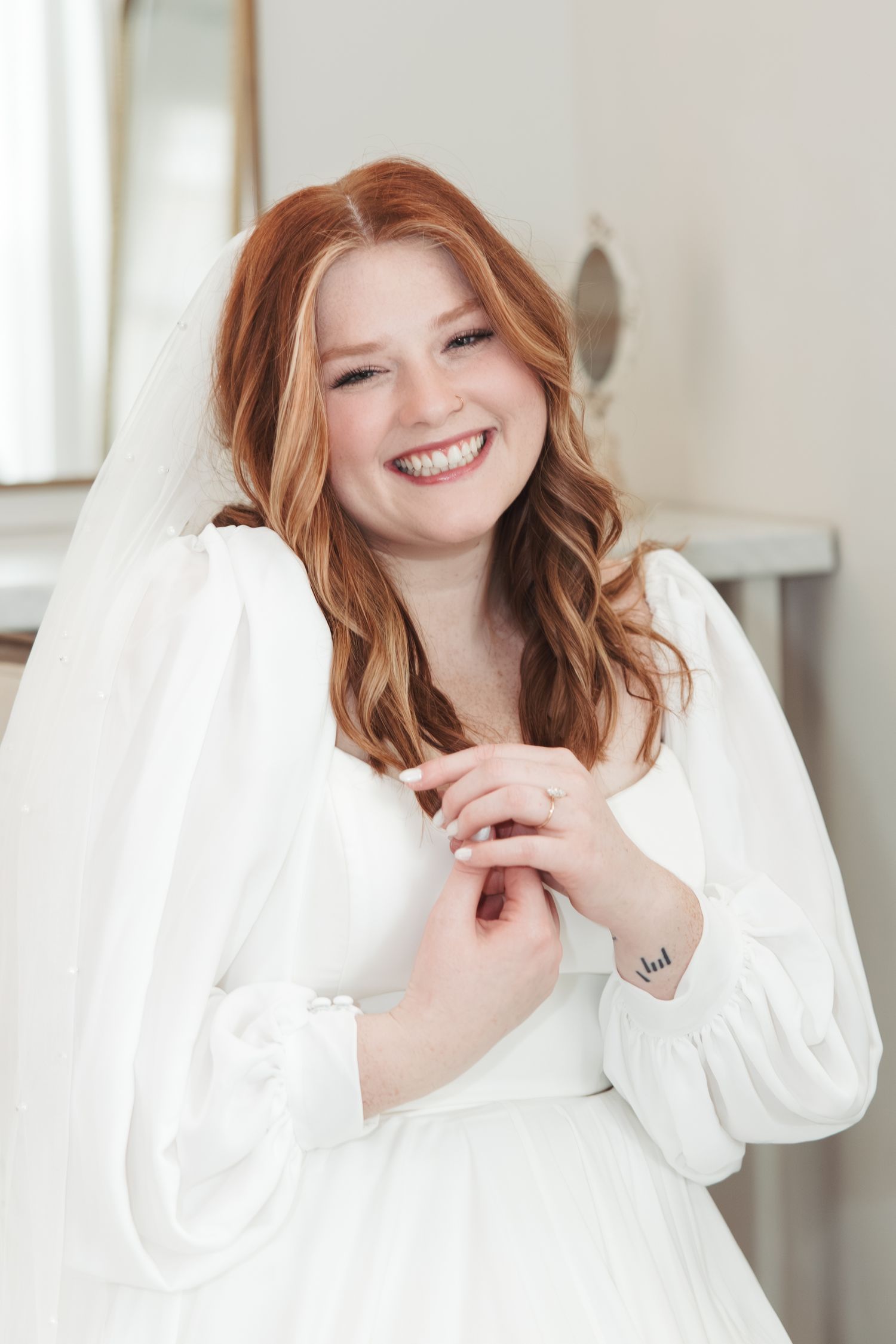 Bride in white long-sleeve dress with flowing veil smiles joyfully.
