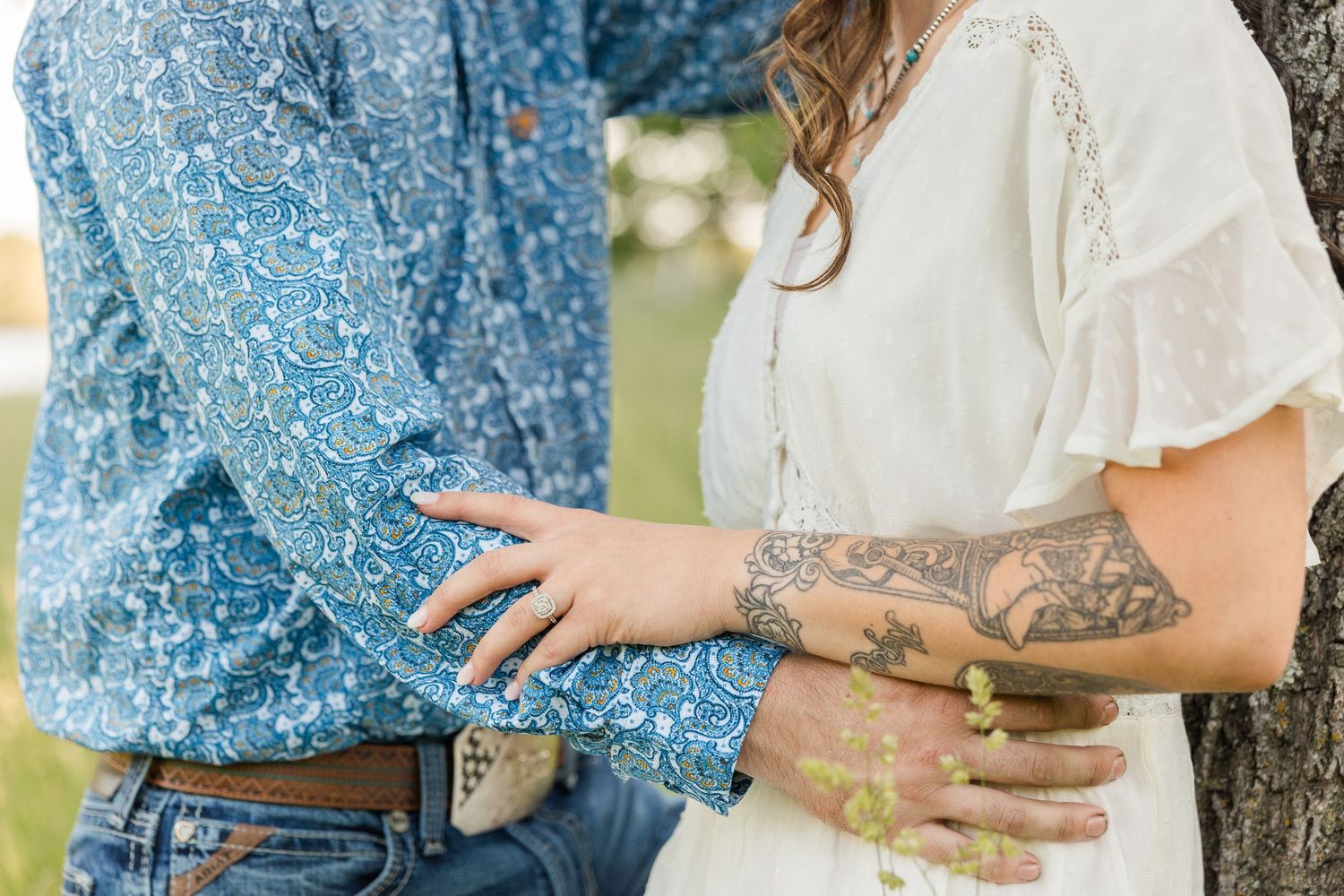 A close-up view of a couple embracing outdoors, with visible tattoos and a blue patterned shirt.