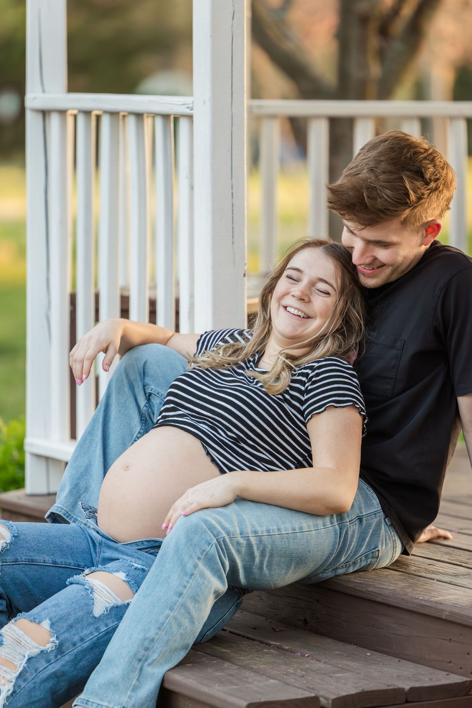 A couple relaxes together on a white porch during a casual maternity session.