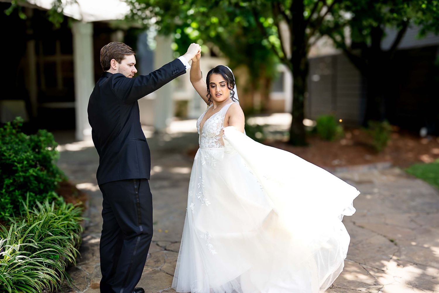Groom in black suit twirling bride in white lace ballgown wedding dress outdoors.