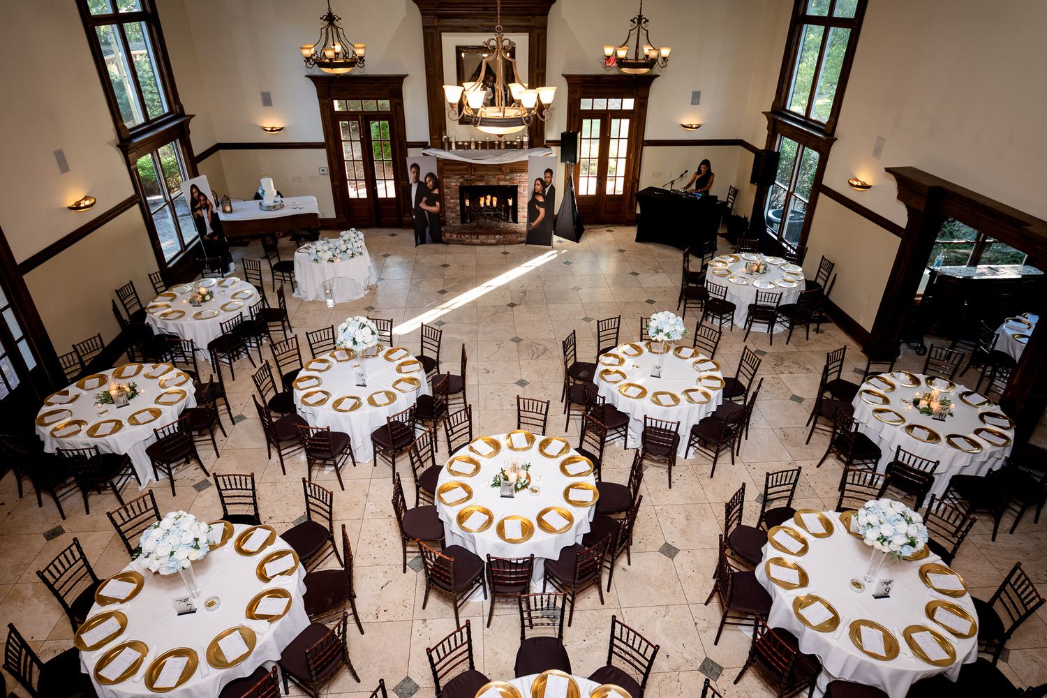 Elegant wedding reception hall with round tables, gold accents, dark chiavari chairs, and a grand fireplace centerpiece Carl House wedding