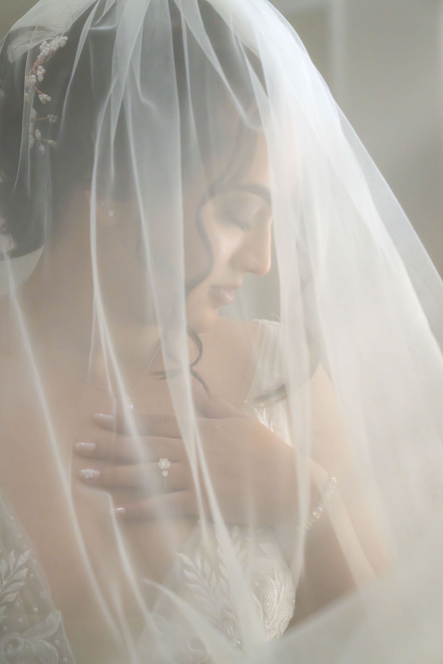Bride in lace wedding dress covered by flowing white veil, elegant bridal portrait photography.