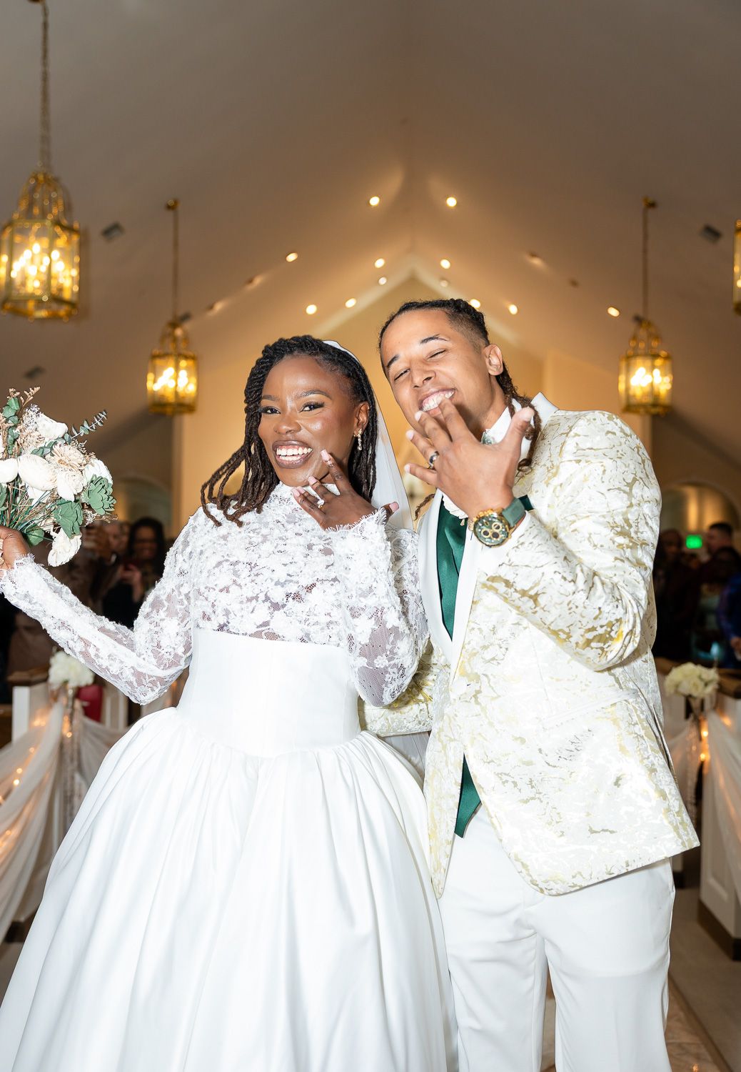 Happy newlyweds celebrate at Pristine Chapel, bride in lace gown holding bouquet, groom in gold floral blazer.