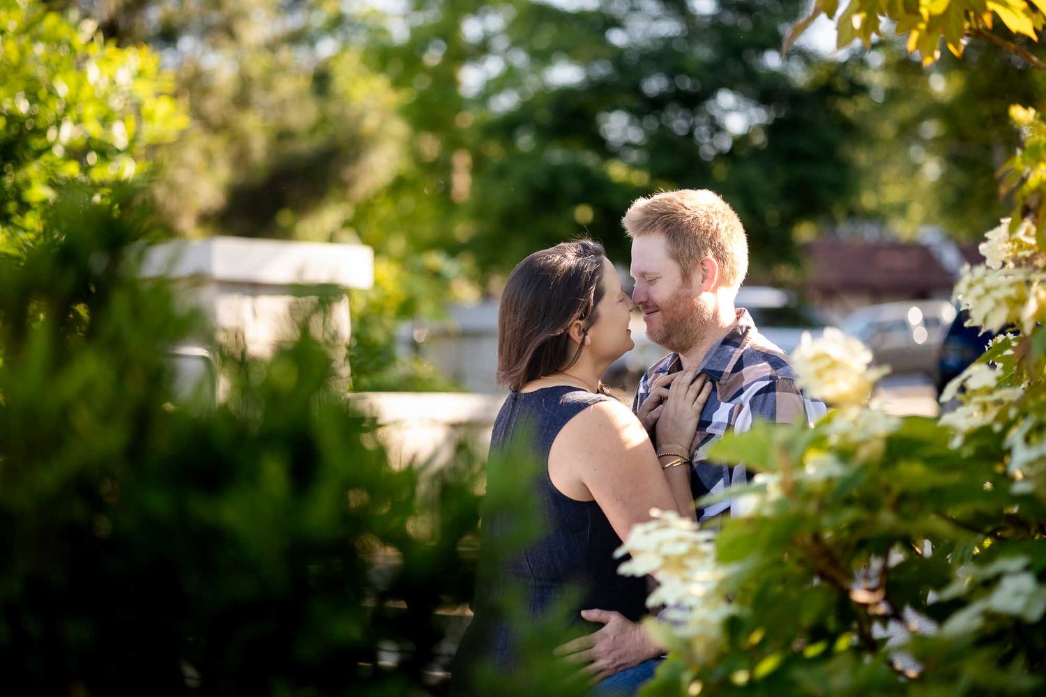 Couple sharing a romantic moment surrounded by lush green garden foliage in warm sunlight.