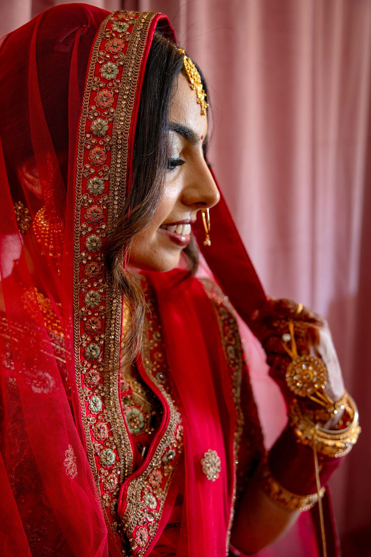 A close-up portrait of a traditional Indian bride wearing a red embroidered wedding sari and intricate gold jewelry.