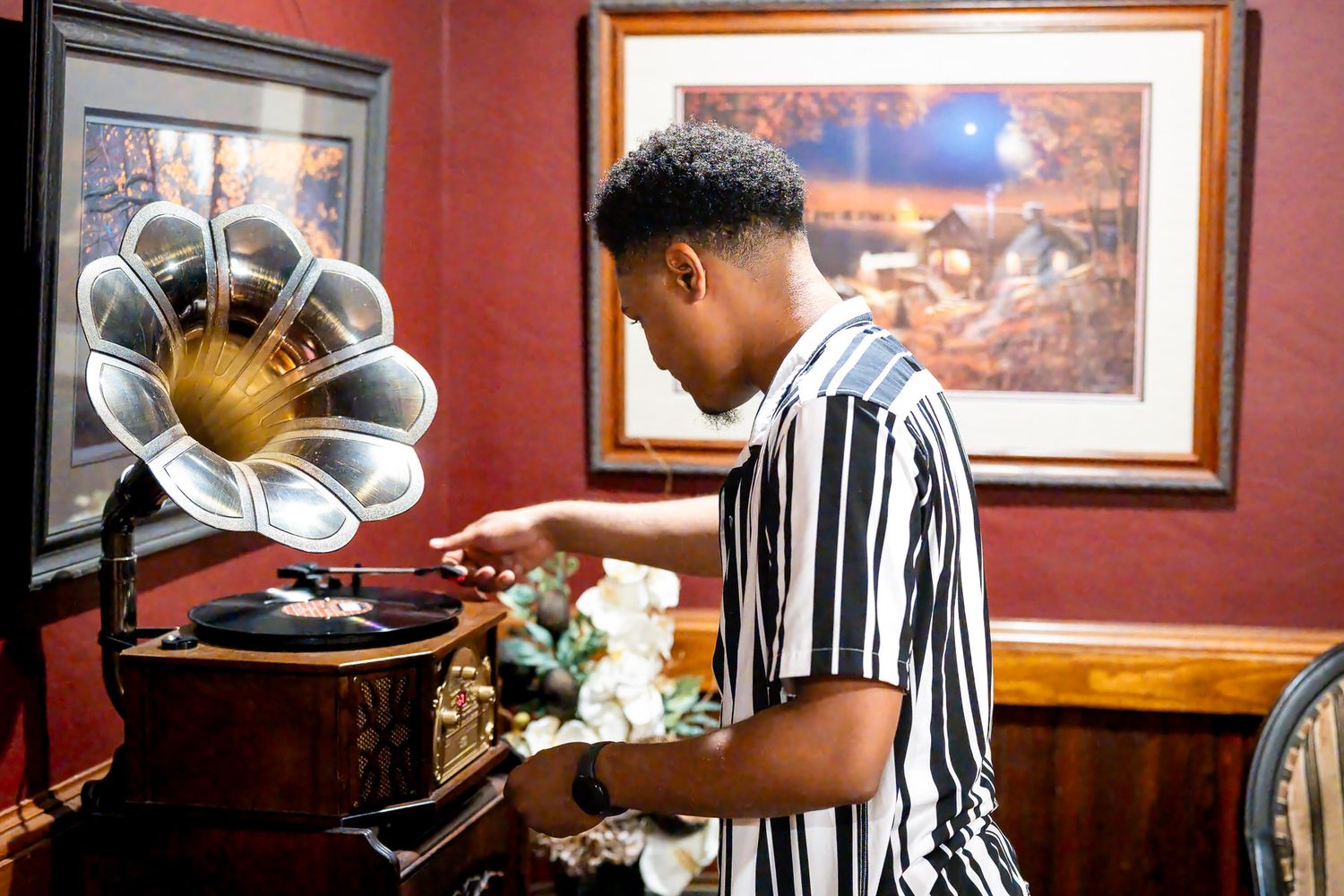 Young man in striped shirt playing a vintage gramophone with vinyl record in a classic red-walled room.