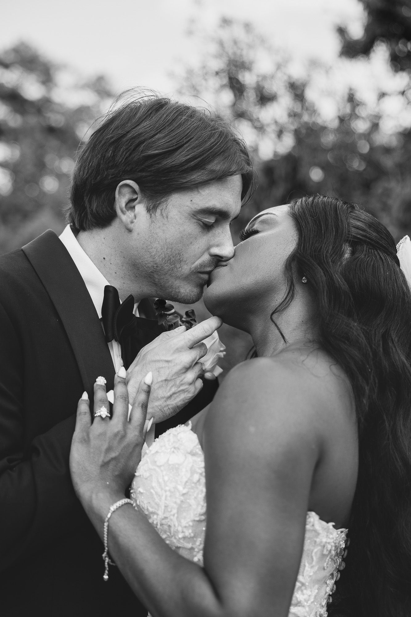 Black and white photo of a bride and groom sharing a romantic kiss on their wedding day outdoors.