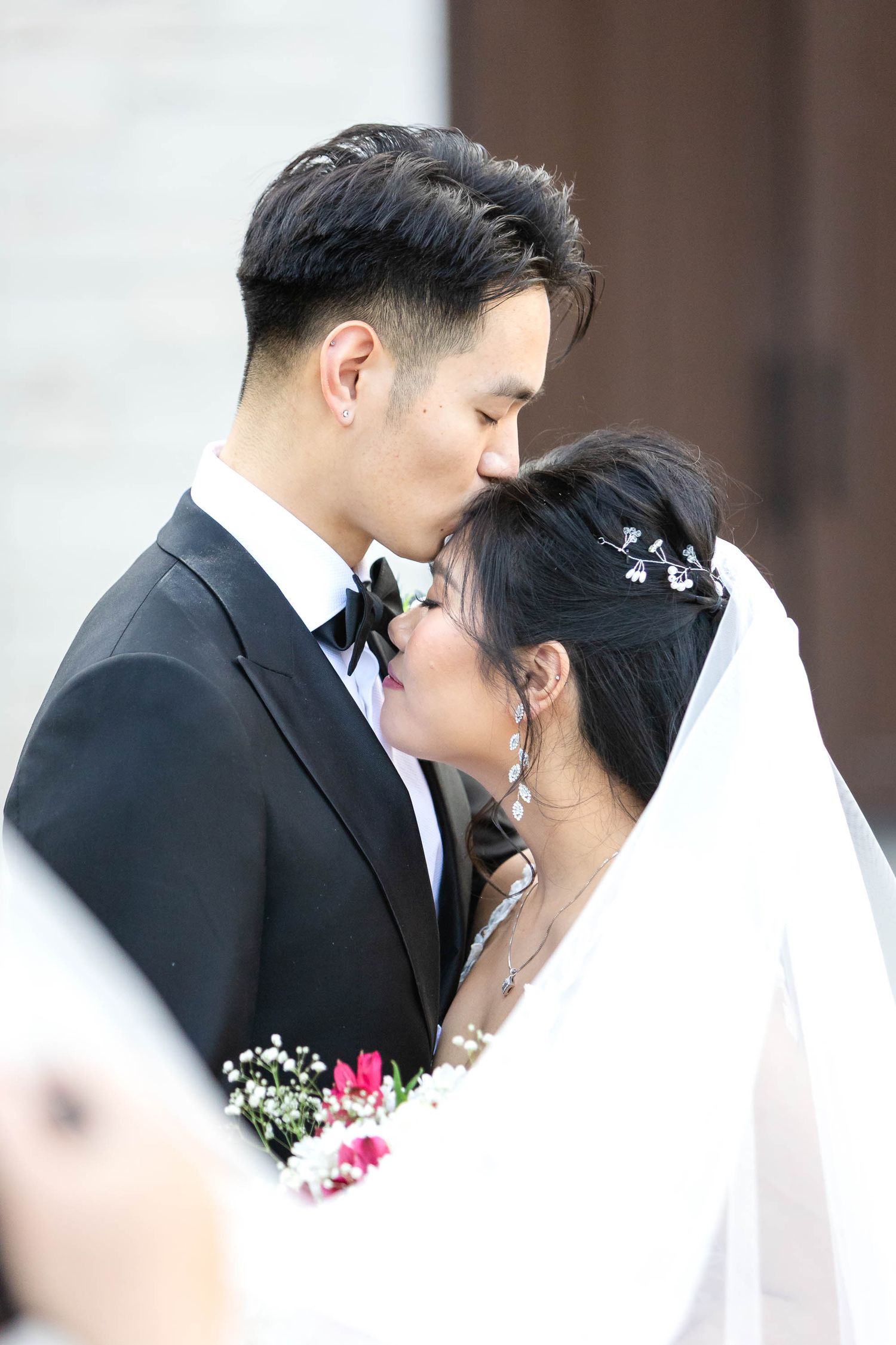 Asian bride and groom share a kiss at their wedding ceremony, with the bride holding a bouquet of flowers.