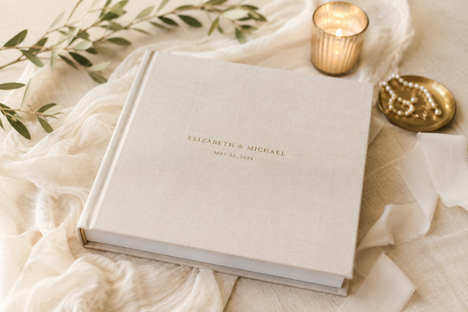Elegant linen wedding photo album personalized with gold foil names and date, styled with candle and greenery.