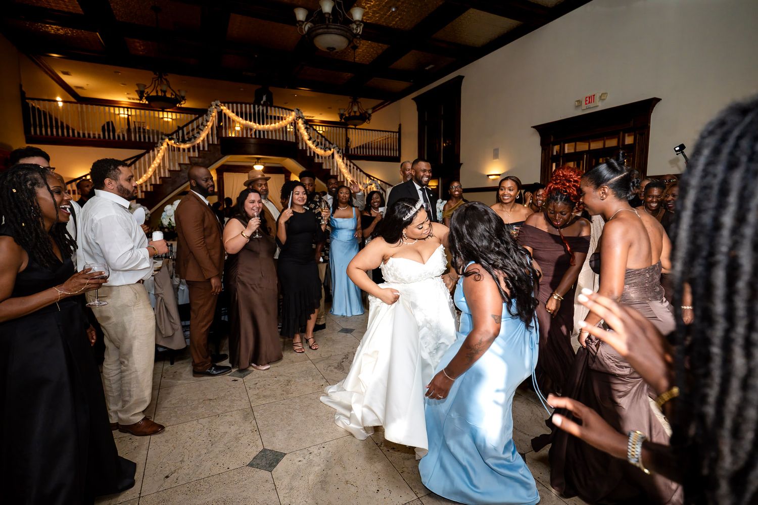Bride in white gown dances joyfully with guests in blue dresses at elegant wedding reception celebration.