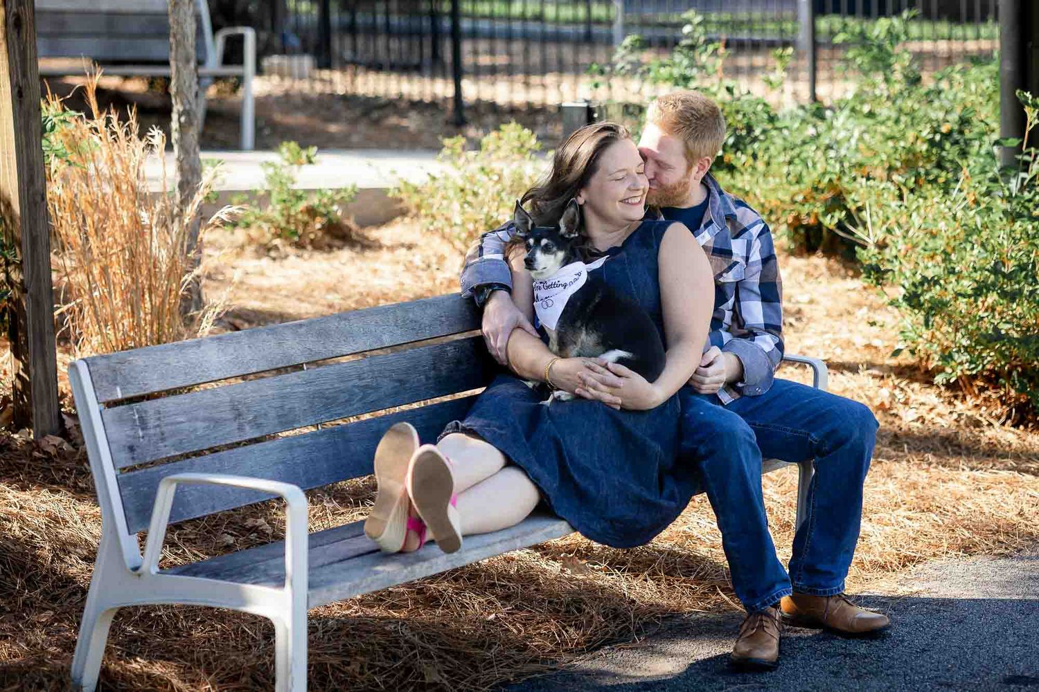 Couple sitting closely on a white park bench, sharing a romantic moment outdoors on a sunny day.