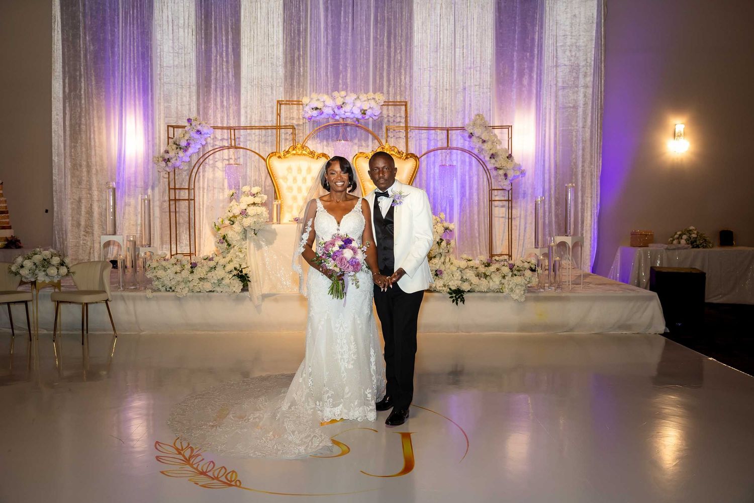 Newlyweds posing together on dance floor at luxurious wedding venue with gold arch backdrop.