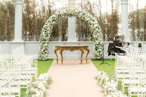 An elegant outdoor wedding ceremony setup with white chairs and floral arrangements in a garden setting.