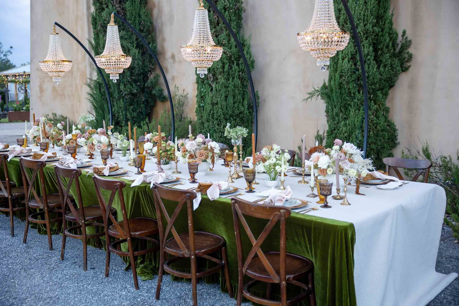 Elegant outdoor wedding reception table with green velvet runner, chandeliers, and floral centerpieces.