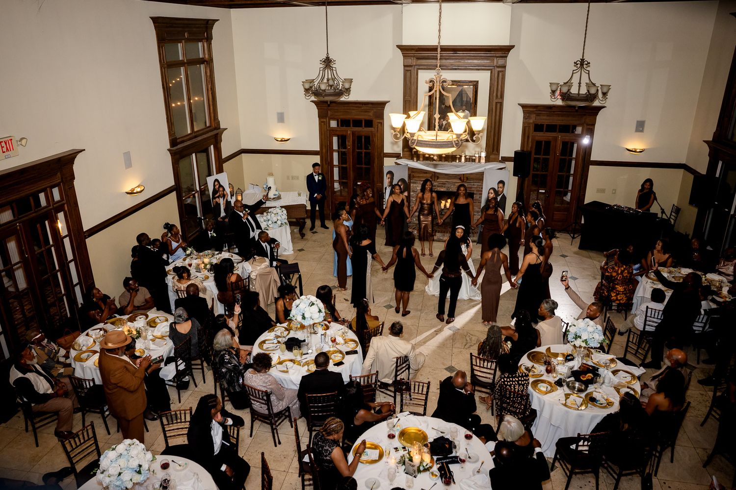Aerial view of wedding reception in elegant ballroom with round tables and guests dancing on marble floor.