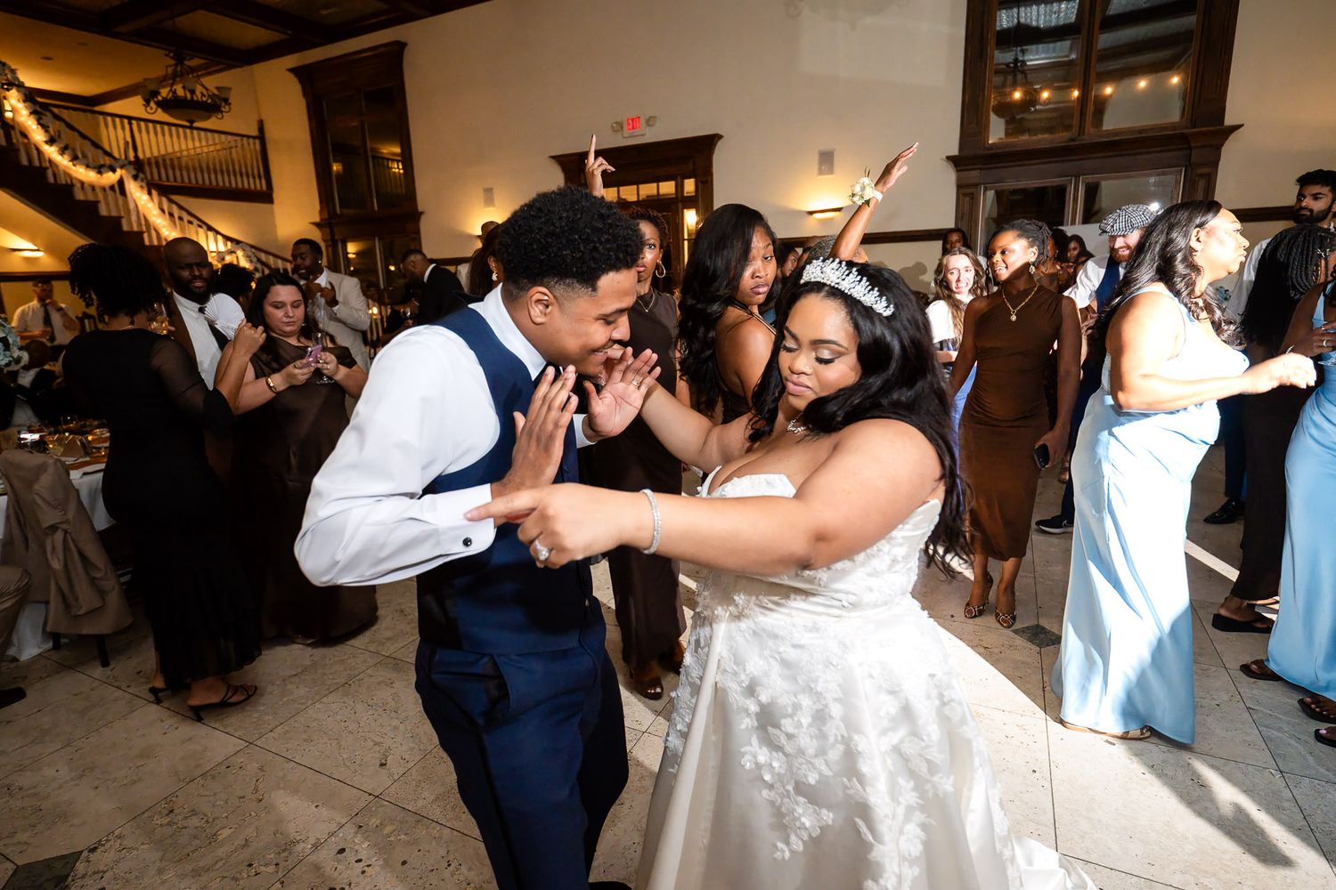 Bride and groom dancing joyfully at wedding reception with guests celebrating in elegant venue.
