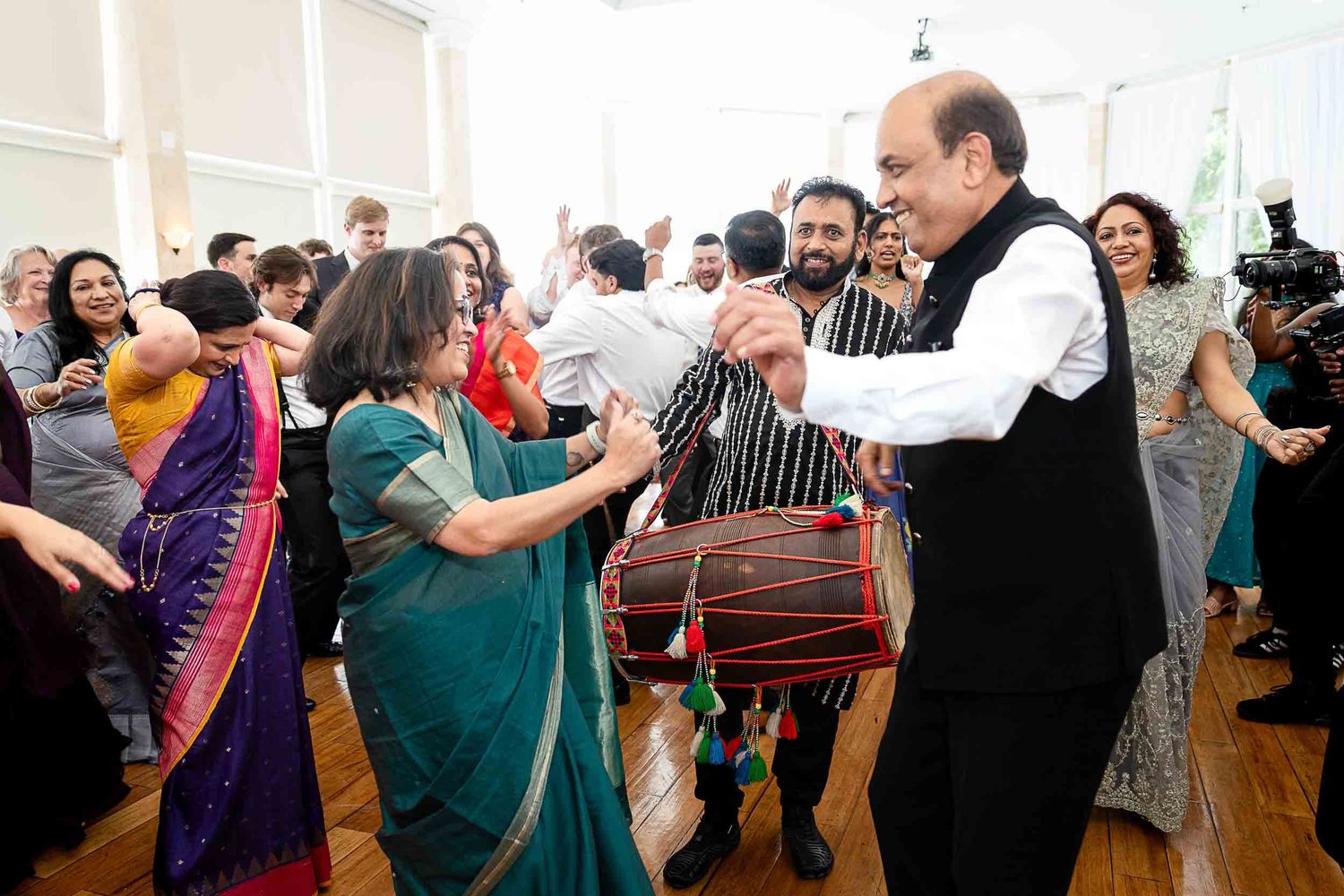 Guests celebrate at Indian wedding reception with traditional dhol drumming and dancing in bright festive attire.