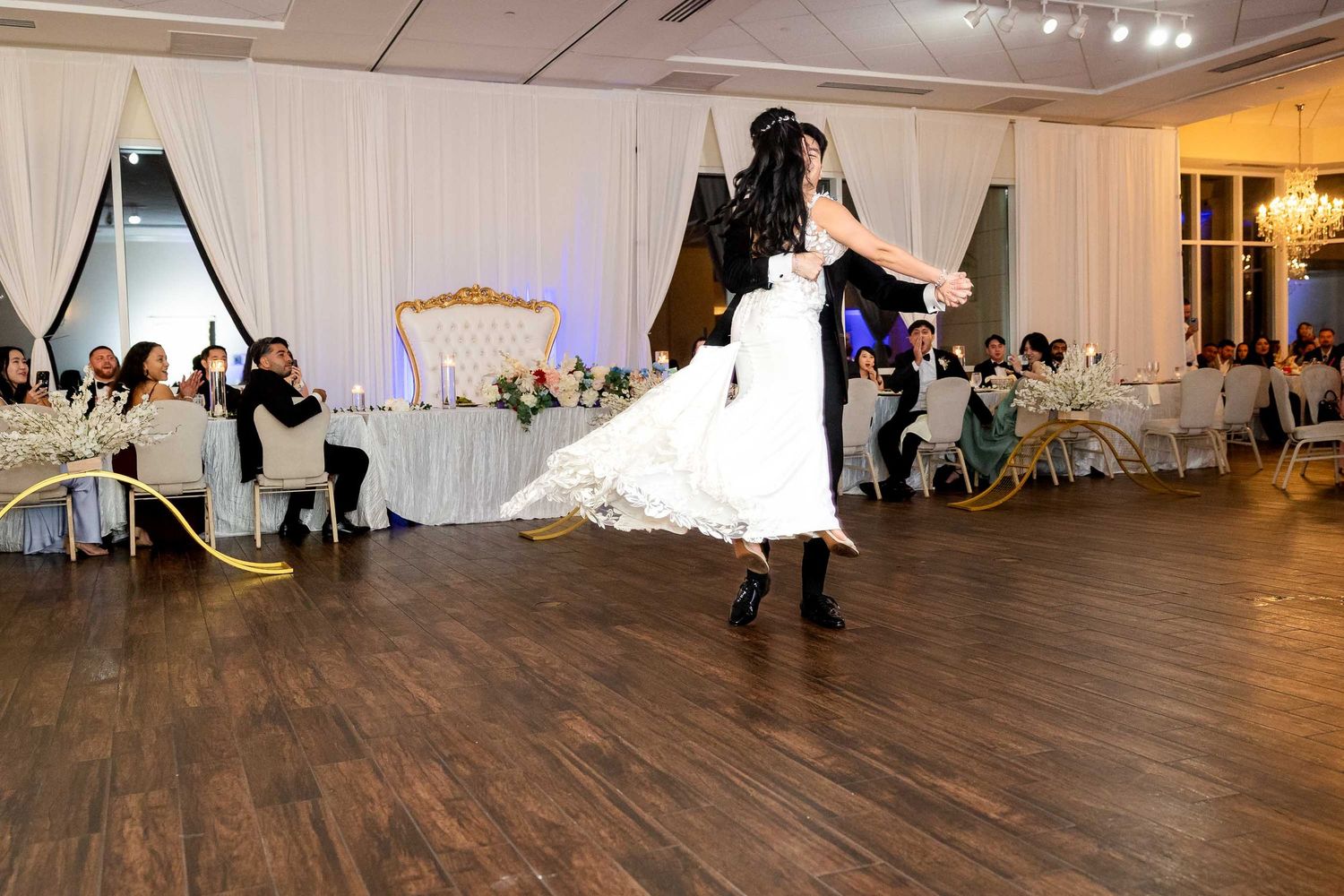 Bride and groom share their first dance on a wooden dance floor at an elegant wedding reception venue.