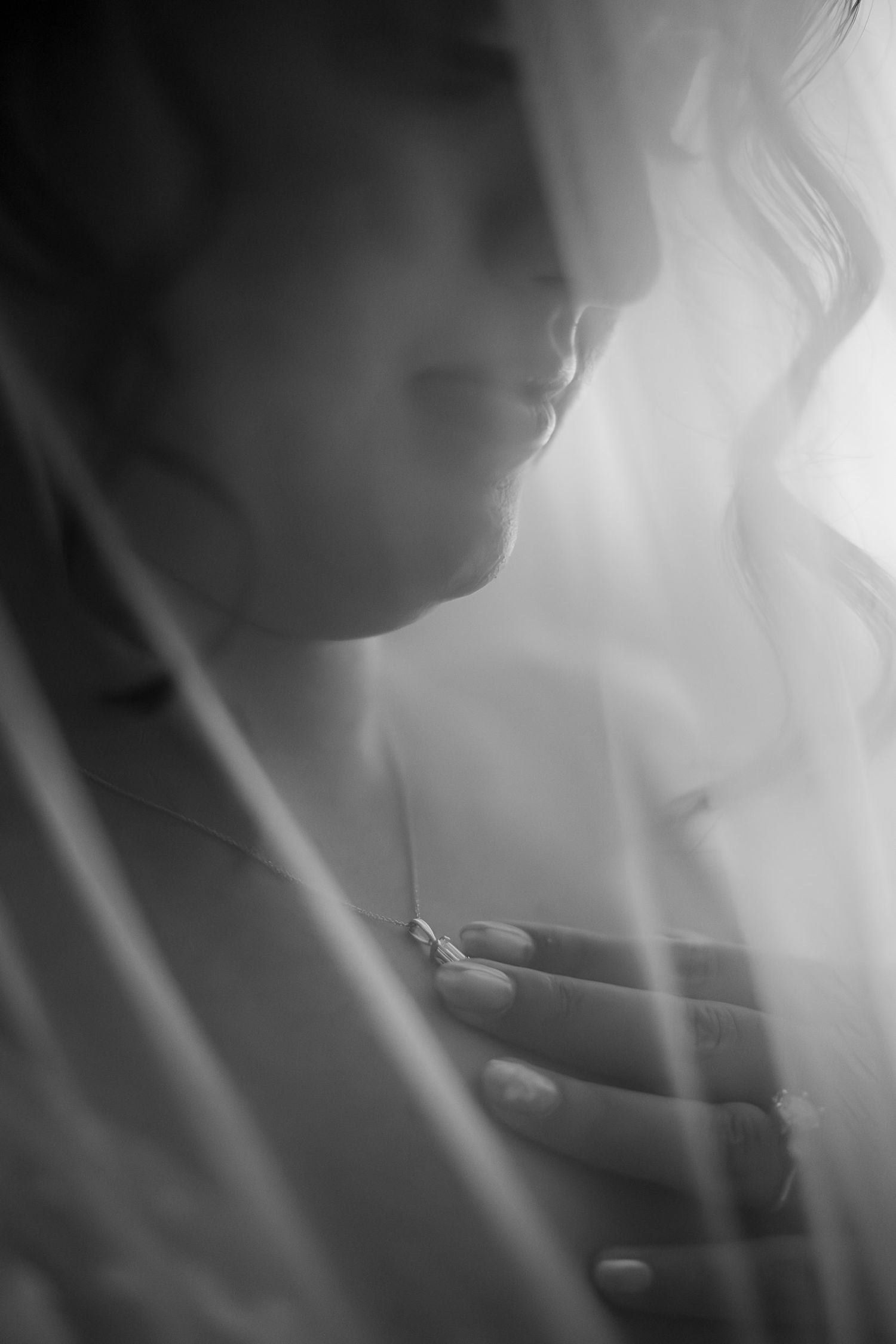 Black and white bridal portrait of a woman draped in a sheer veil, her hand gracefully resting on her chest.