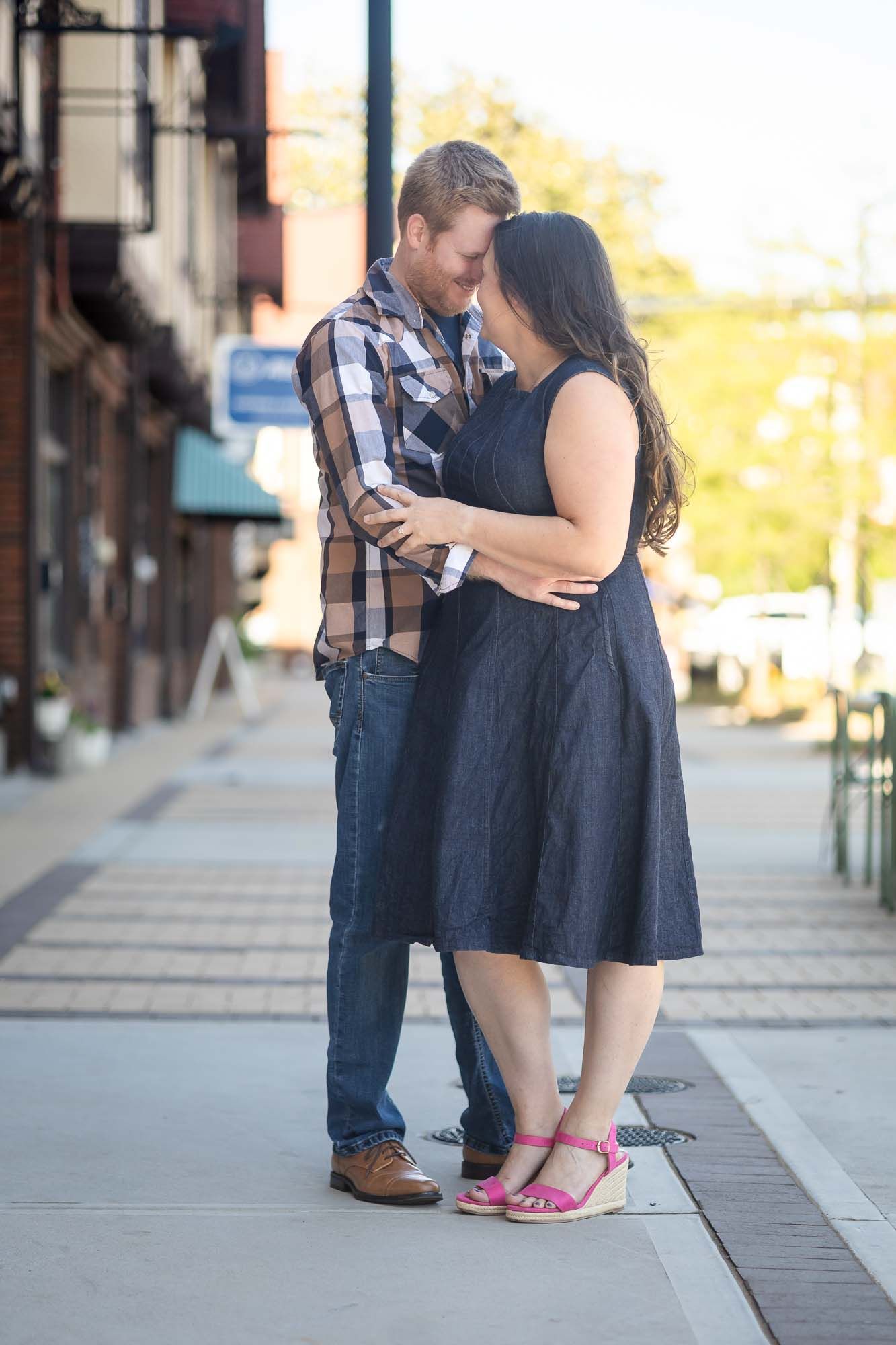 Romantic couple sharing an intimate moment on a city sidewalk, woman in navy dress and pink wedges.