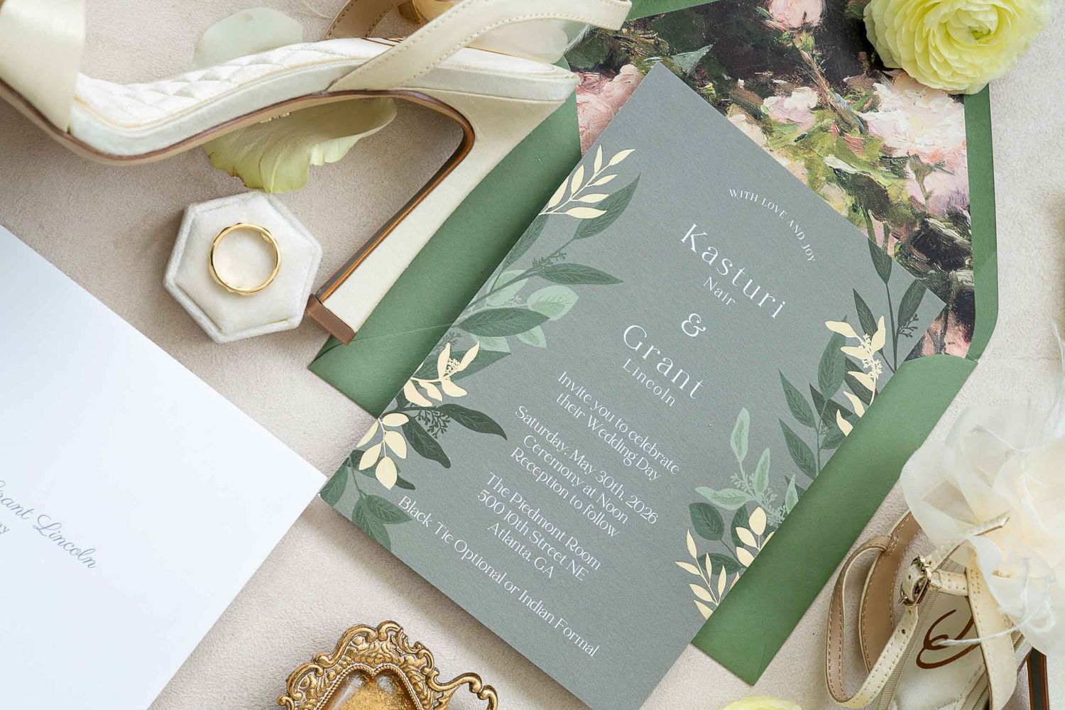Elegant green botanical wedding invitation suite with floral accents, gold ring, and ivory accessories on a soft background.
