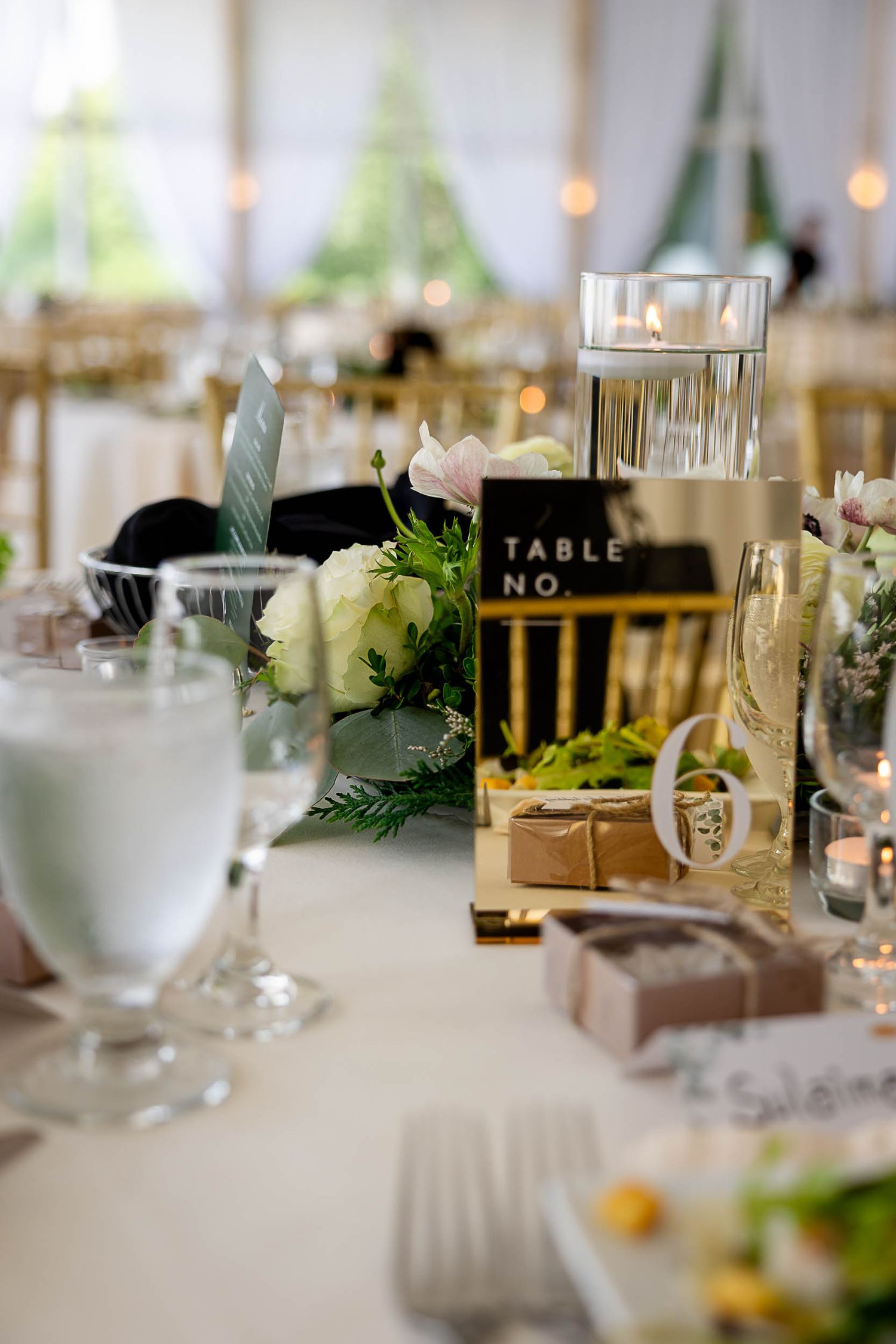 Elegant wedding reception table setting with floral centerpiece, floating candle, and gold table number sign.