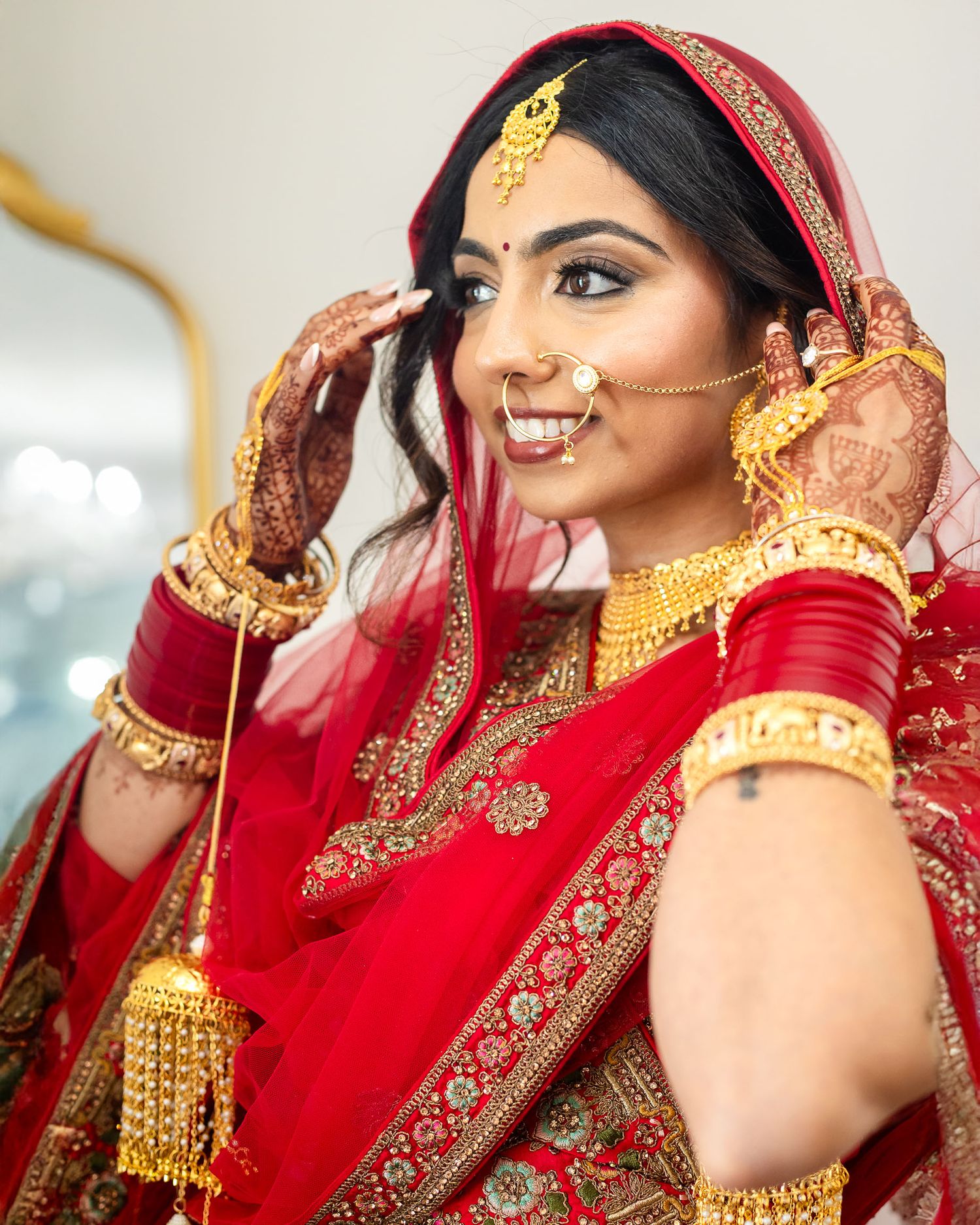 Traditional Indian bridal attire featuring a red and gold embroidered sari with ornate jewelry and henna decorated hands.