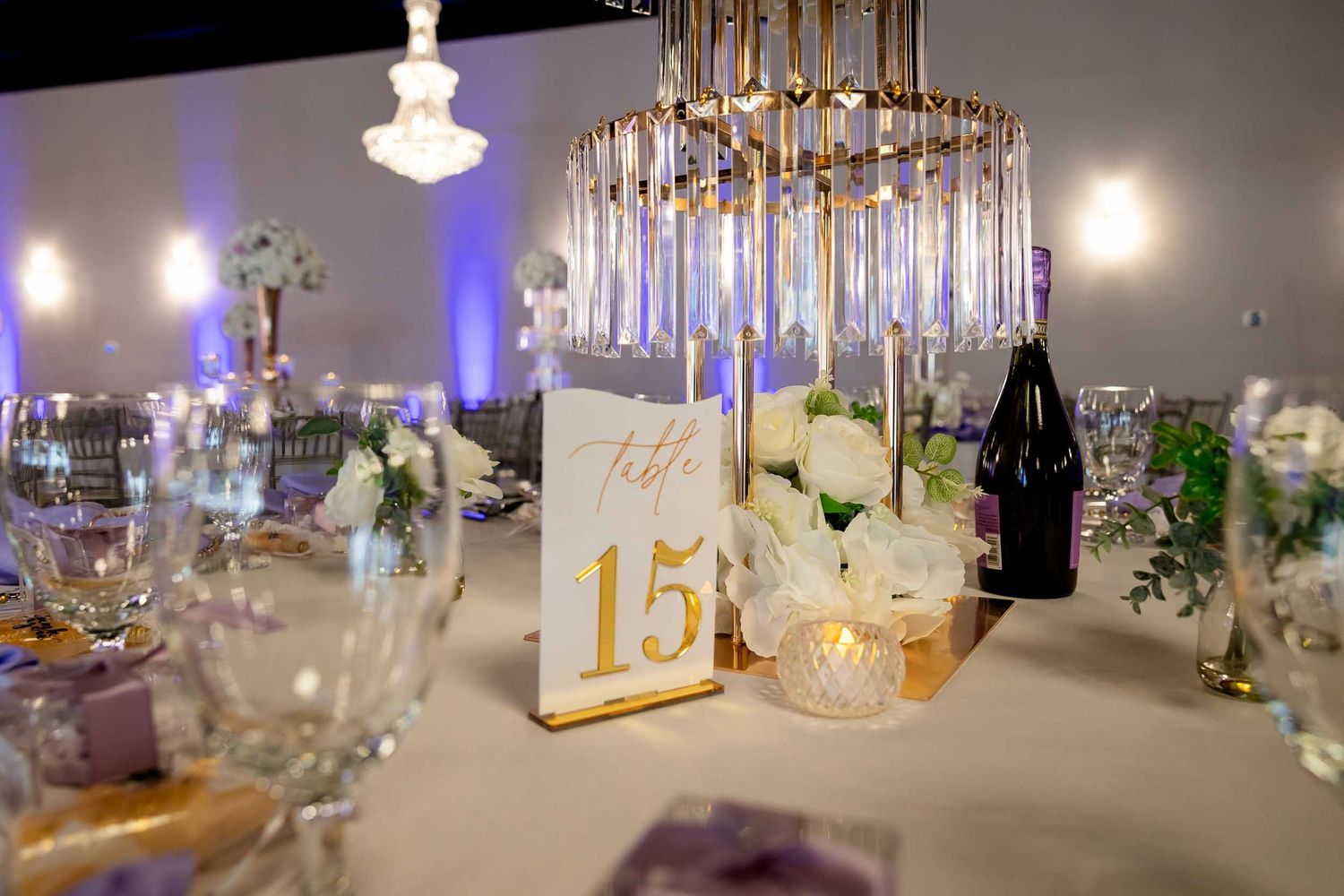 Elegant wedding reception table 15 with gold candelabra, white roses, crystal glasses, and purple ambient lighting.