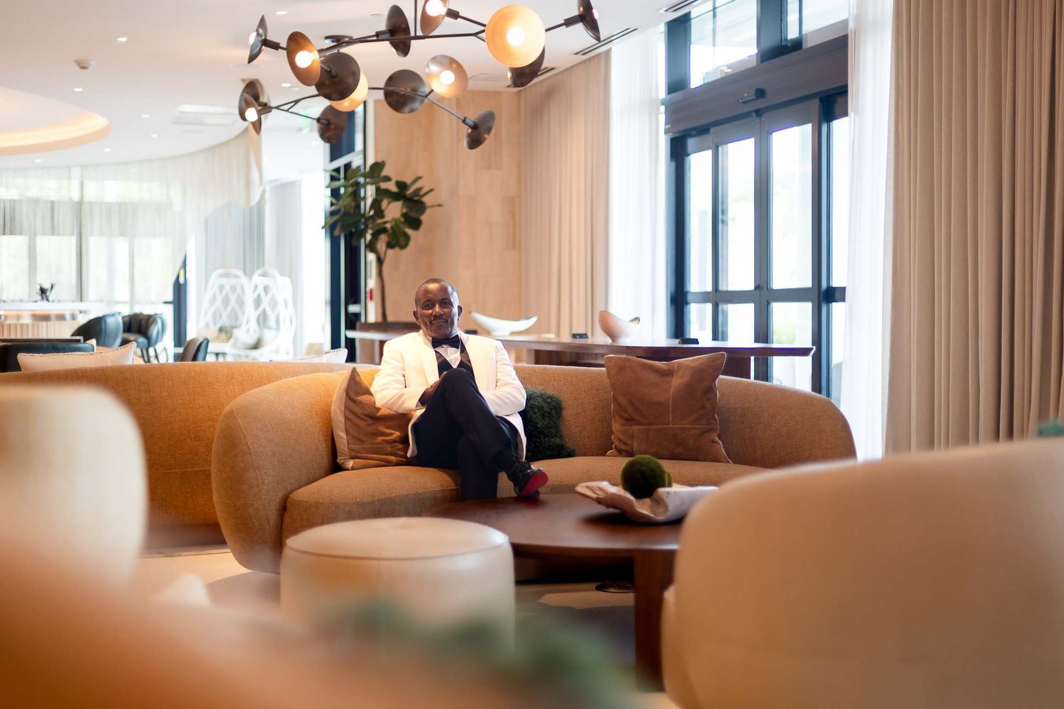 Elegant man in suit relaxing on leather sofa in modern hotel lobby.