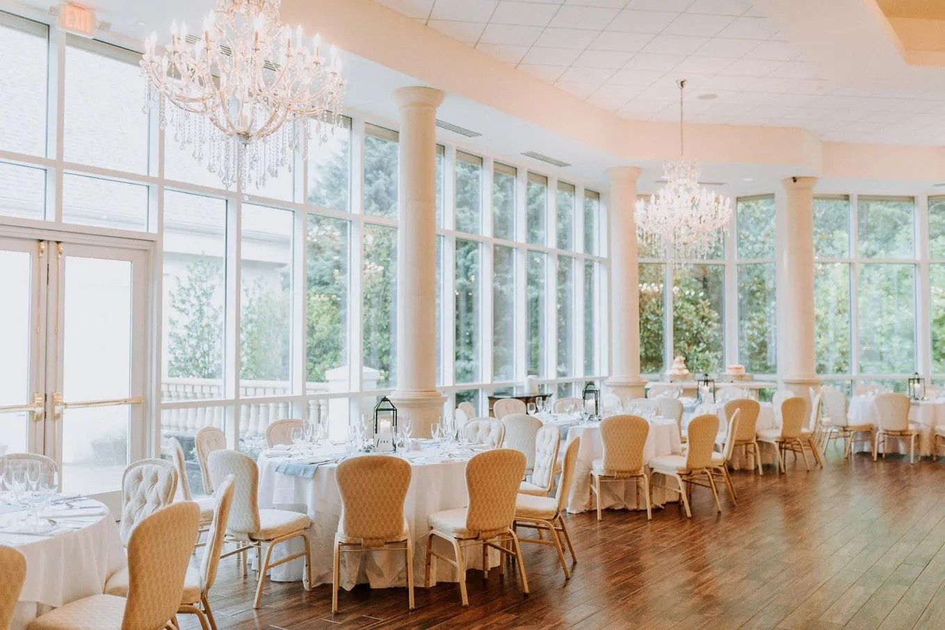 Elegant banquet hall with crystal chandeliers, white tables, and expansive windows overlooking lush greenery.