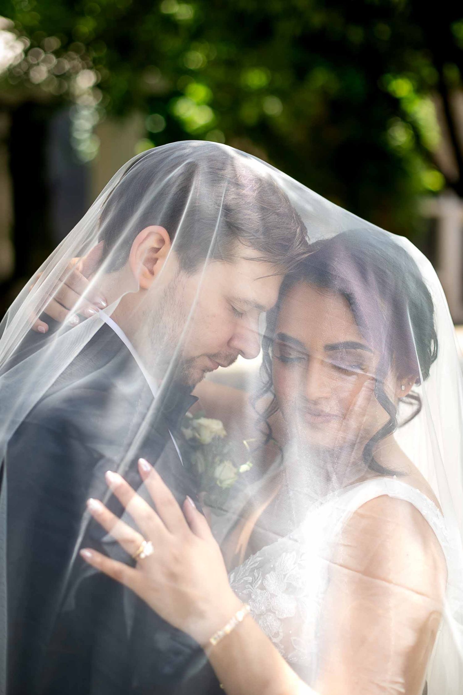 Bride and groom share an intimate moment under a flowing wedding veil outdoors.