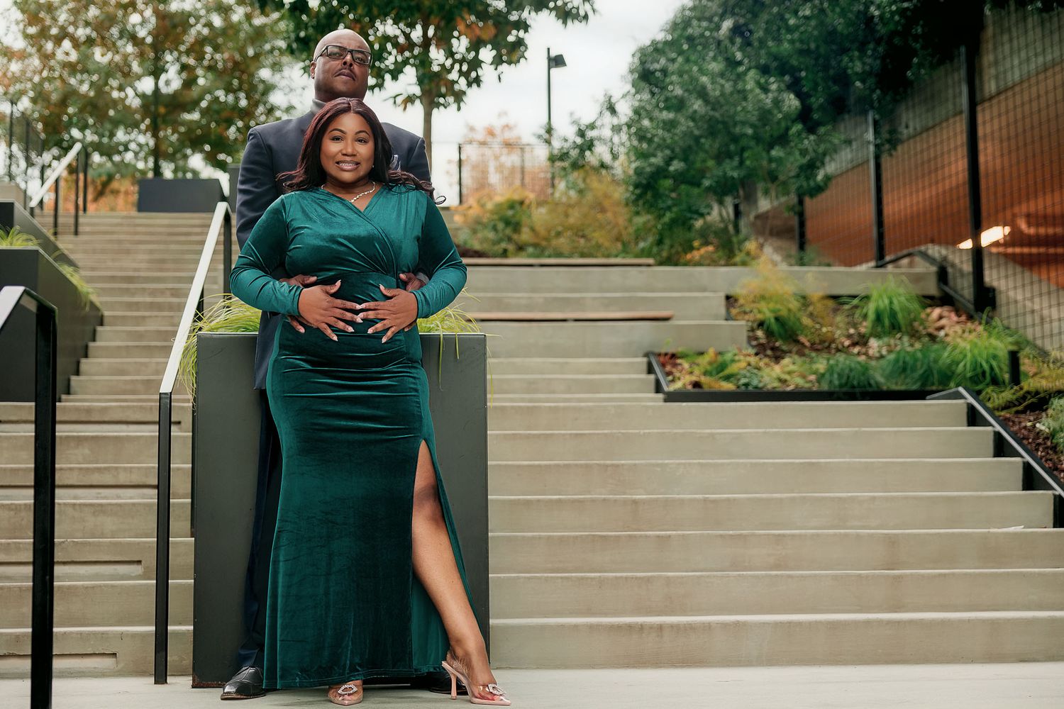 Pregnant woman in emerald green gown poses with partner on outdoor steps during maternity photoshoot.