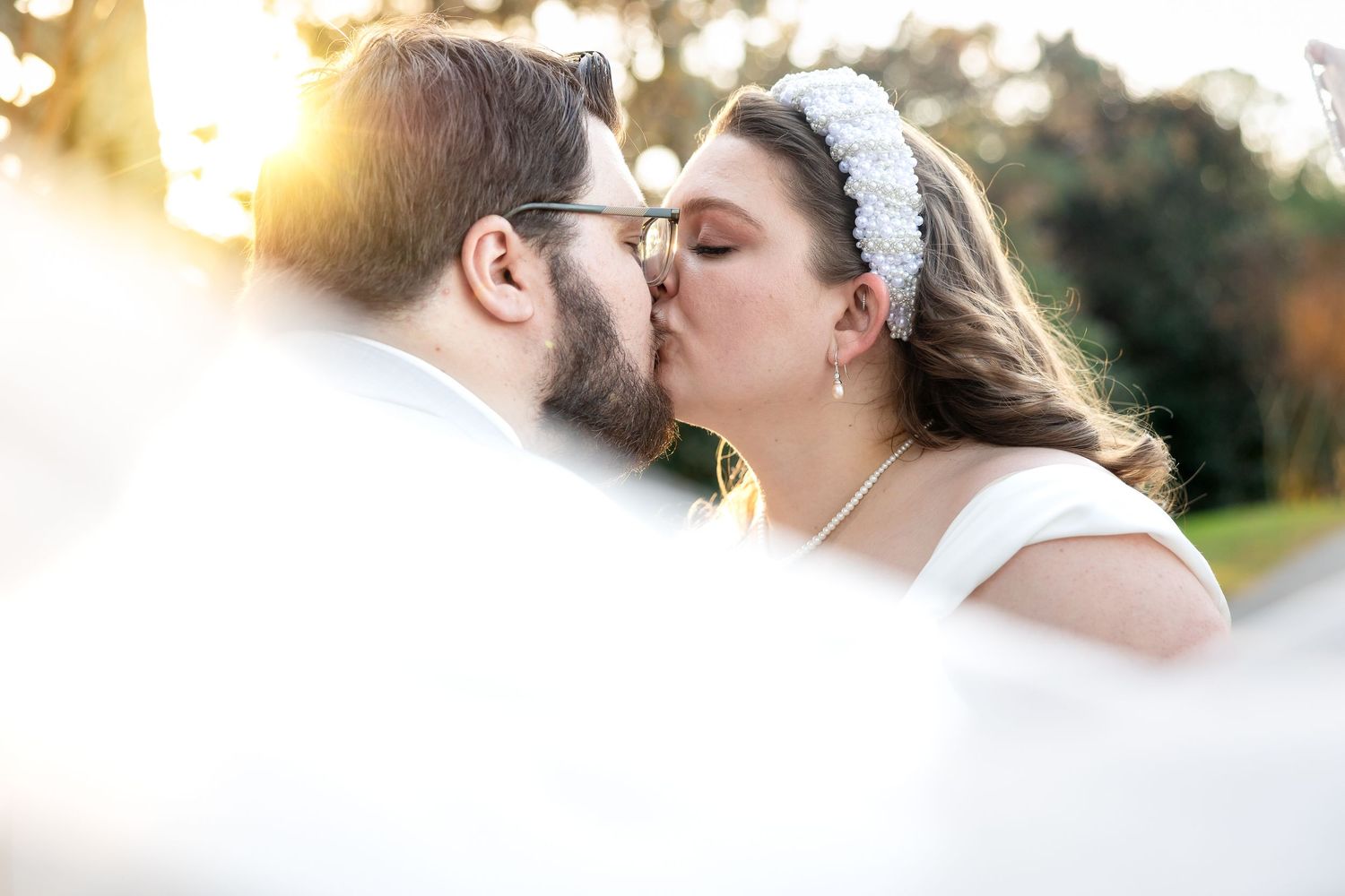Bride and groom sharing a romantic kiss outdoors during golden hour sunset at their wedding ceremony.