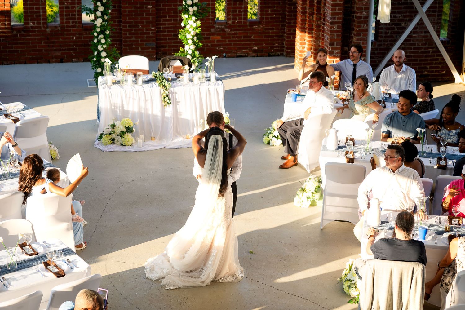 Bride and groom share first dance at elegant outdoor wedding reception with white-draped tables and seated guests.