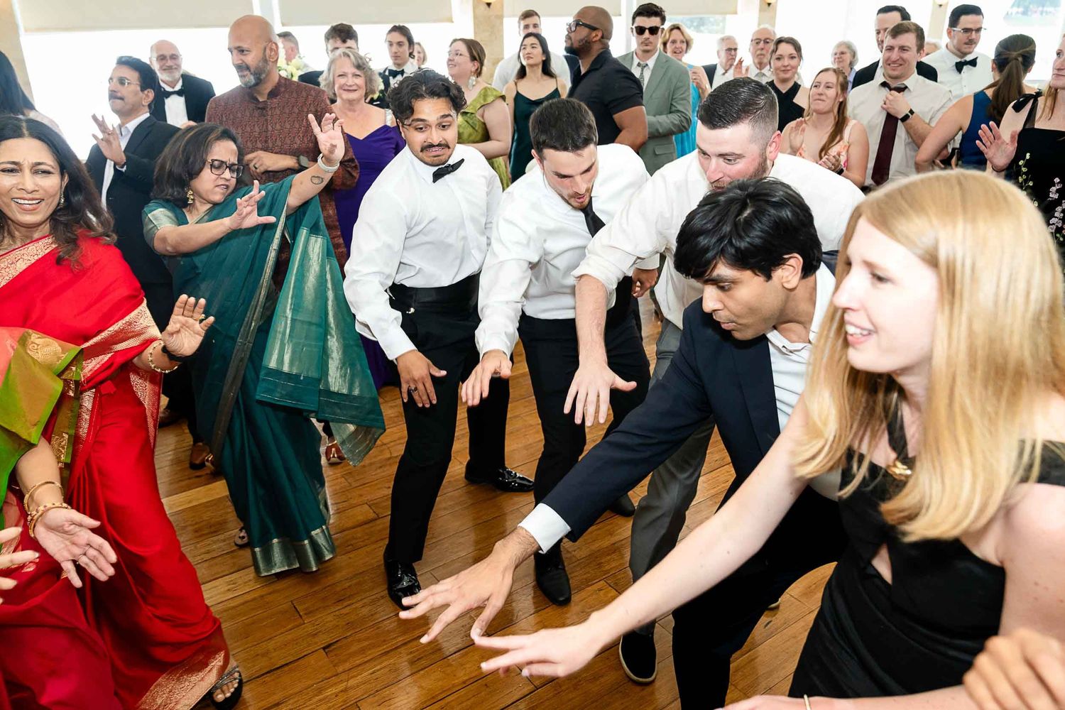 Guests enjoying a lively group dance at a wedding reception on a wooden dance floor.