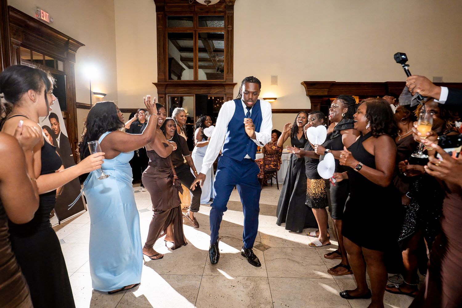 Groom in blue suit dancing joyfully with guests at wedding reception celebration.