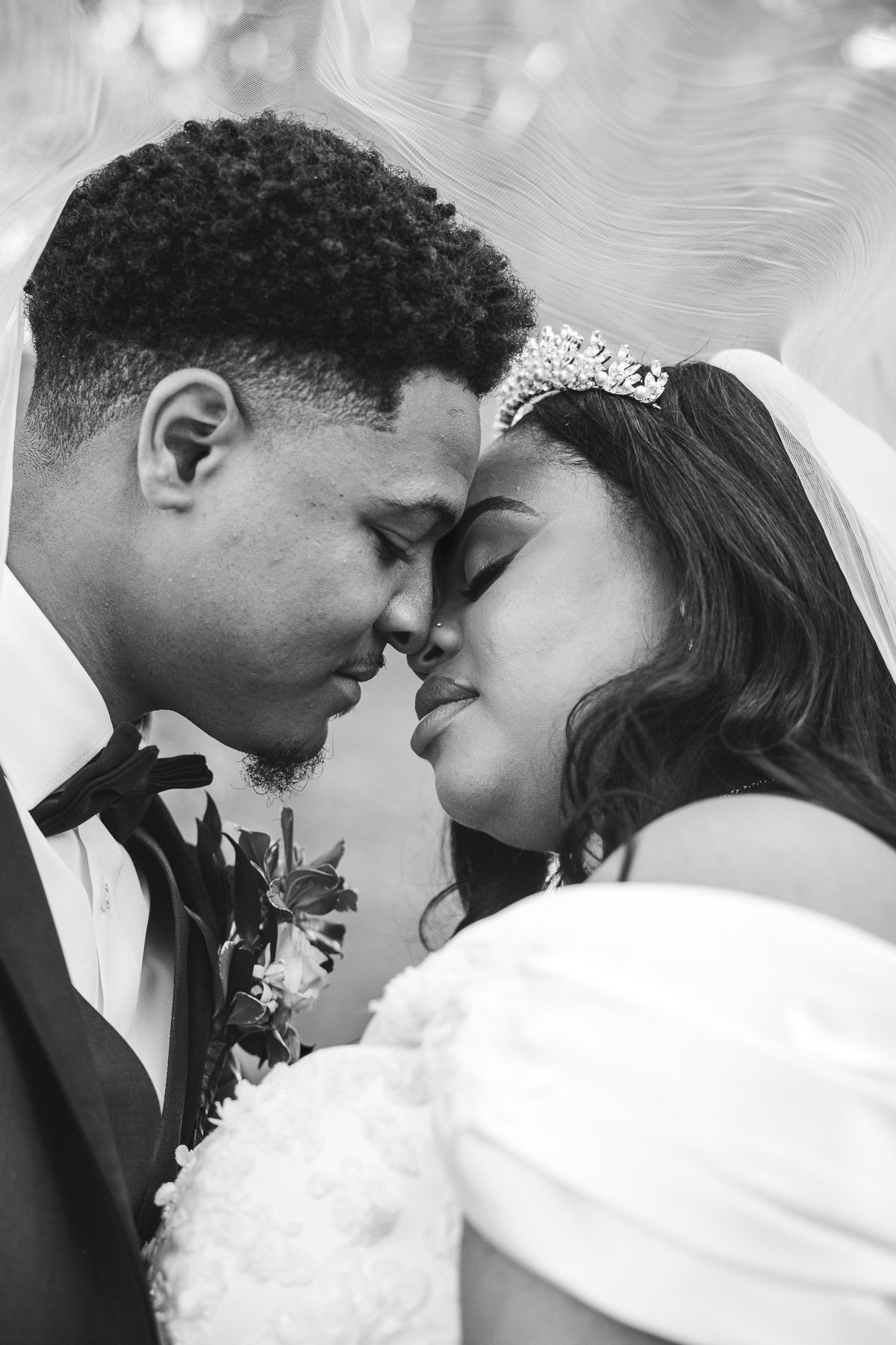 Black and white photo of a bride and groom touching foreheads tenderly on their wedding day.