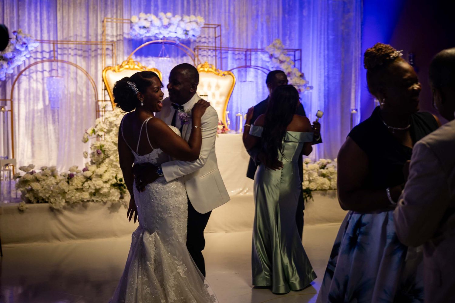 Bride and groom share first dance embrace in stunning white and gold decorated wedding venue.