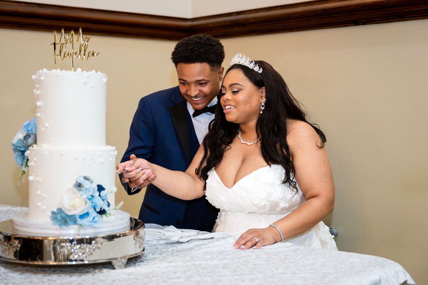 Bride and groom cutting their white wedding cake with blue floral accents at their elegant wedding reception.